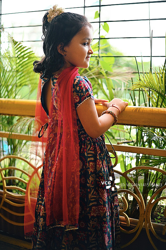 可爱的印度女孩穿着传统服装从阳台向外看图片素材