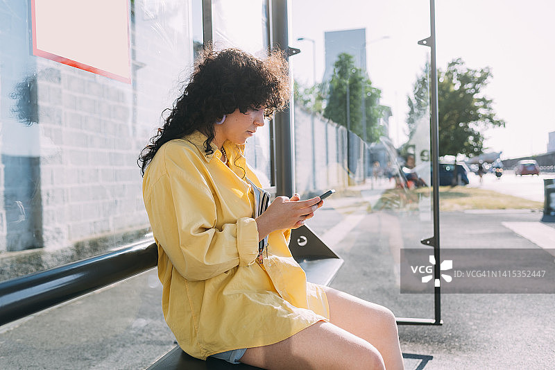 年轻女子坐在公交车站用智能手机图片素材