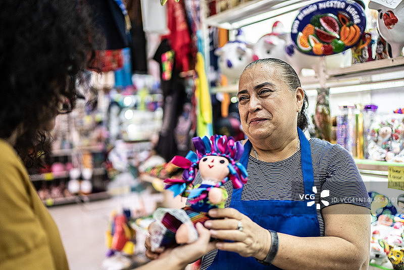 中年妇女在礼品店从高级妇女手中接过墨西哥娃娃图片素材