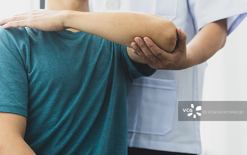 一个肩膀疼的男人去看医生，医生诊断病人的胳膊疼和肩膀疼。物理治疗和康复的概念。图片素材
