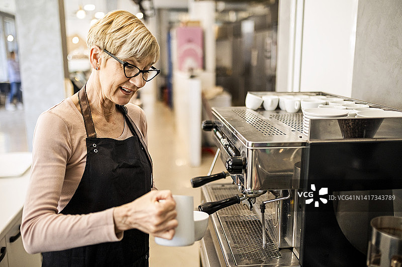 成熟的女咖啡师在她的咖啡柜台为顾客准备咖啡图片素材