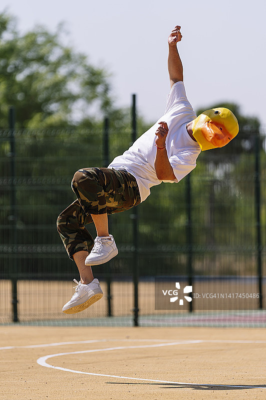 一个戴着动物面具的男子在阳光明媚的日子里在运动场上跳跃图片素材