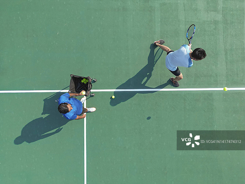 无人机视角的运动训练亚洲中国网球运动员在教练指导下，直接在网球场练习发球图片素材