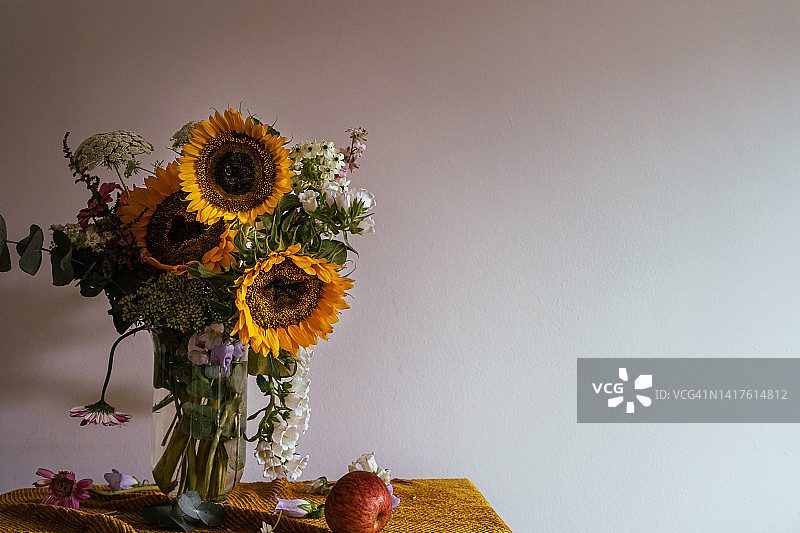 静物的秋天花束，新鲜的向日葵和凋谢的花在玻璃花瓶，棕色的桌布图片素材