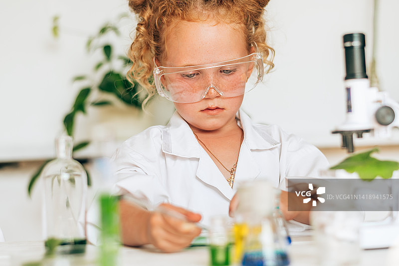 穿着白色制服的红头发小女孩在实验室里做化学实验。回到学校的概念。年轻的科学家。自然科学。儿童的学前和学校教育图片素材