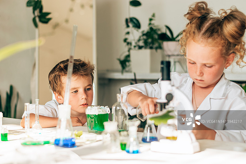 穿着白色制服的小男孩和小女孩在实验室里观察显微镜。回到学校的概念。年轻的科学家。自然科学。儿童的学前和学校教育图片素材