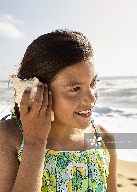 年轻的女孩站在海滩上听贝壳的声音图片素材