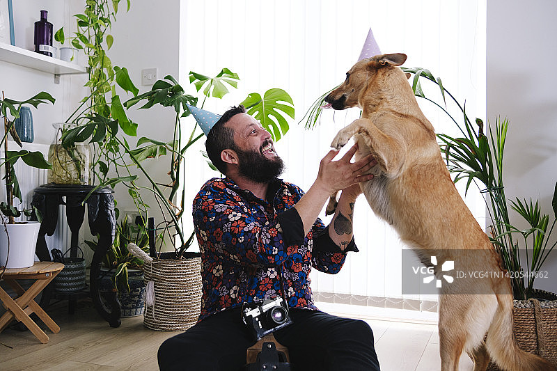 戴着派对帽子的快乐男人在家里和狗狗玩耍图片素材