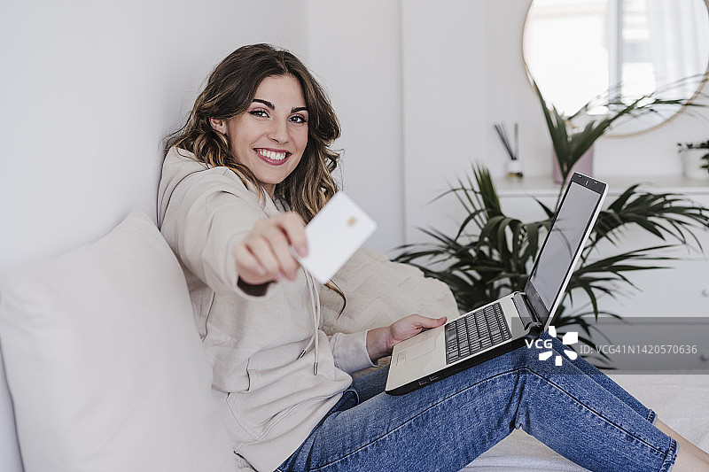 快乐的年轻女子，手提电脑上显示信用卡图片素材