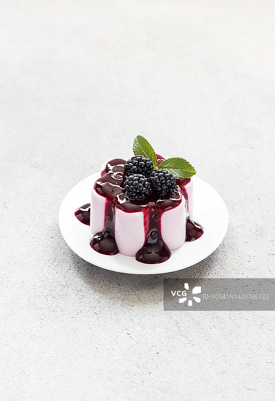 黑莓奶油果冻布丁，意式奶冻配酱，放在盘子里。浅灰色背景图片素材