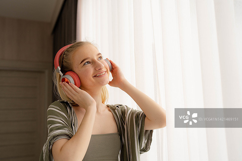 快乐的青少年女子听音乐通过互联网流与耳机。图片素材