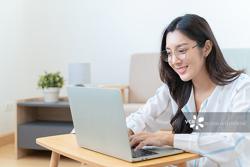 亚洲女性在家里用笔记本电脑工作。图片素材