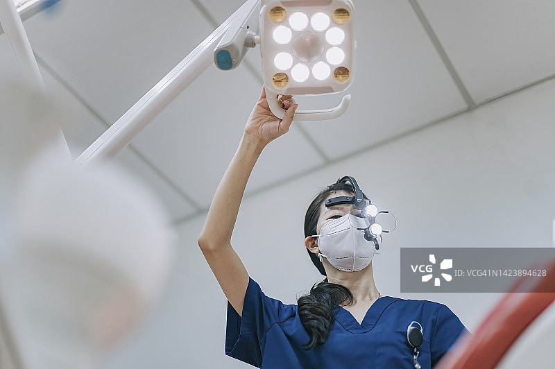 亚裔华人女牙医，用放大镜调节手术光线，从上方观察病人图片素材
