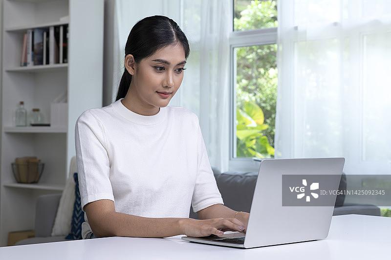 美丽的亚洲妇女在家里使用笔记本电脑。图片素材