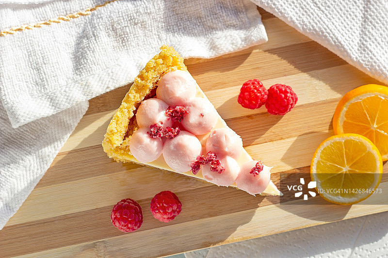 美味的白色和粉色甜覆盆子芝士蛋糕片与新鲜浆果在厨房顶视图的木板上图片素材
