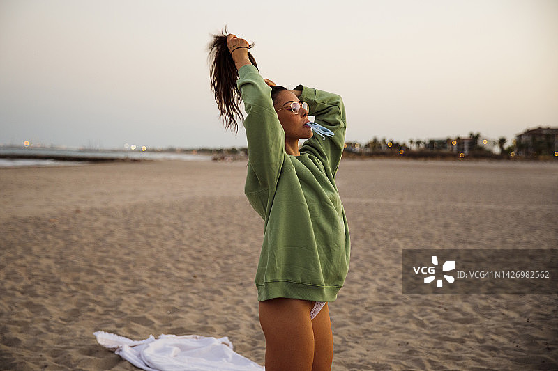 日落时分，海滩上的年轻女子在头发上扎了个马尾图片素材
