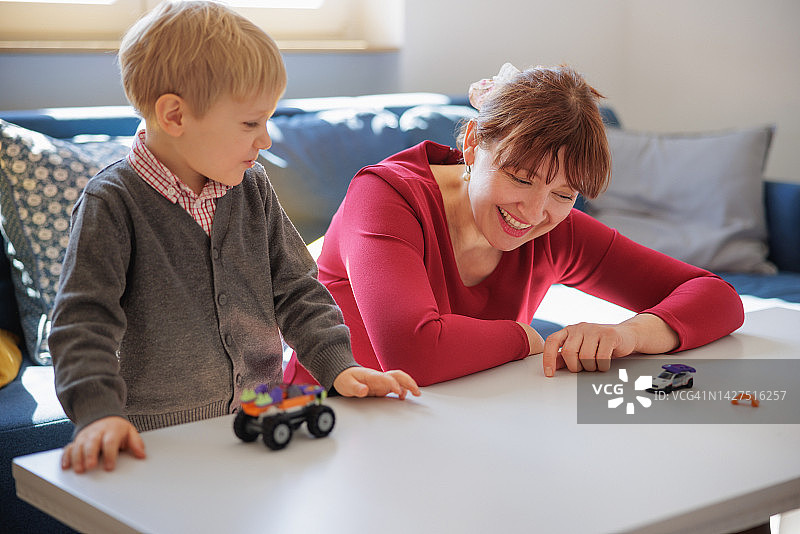 快乐的母亲和她的小儿子在客厅的桌子上玩玩具汽车图片素材
