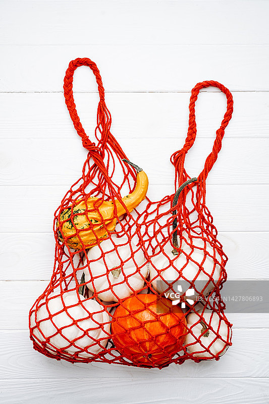 季节性的彩色南瓜在白色背景的红色绳袋。万圣节和感恩节的概念。网状杂货店环保可重复使用购物袋。摄影从上面图片素材