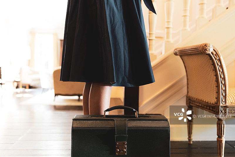 黑人妇女站在公文包旁边，穿着耀斑连衣裙在家里的门厅图片素材