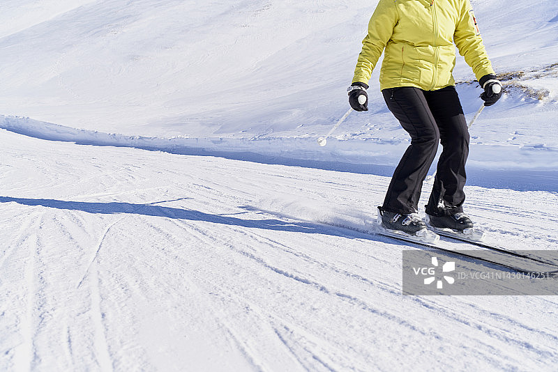 穿着黄夹克黄裤子黑裤子和手套滑雪杖和两块滑雪板在雪地里图片素材