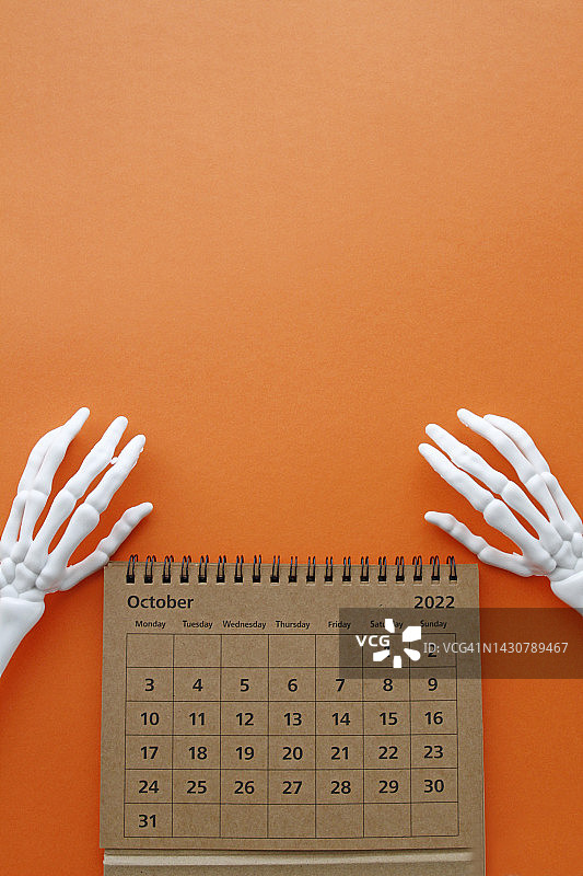 橙色背景上的骷髅手和十月日历图片素材