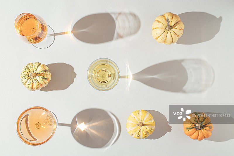 有创意的秋天场景与几个天然的彩色南瓜，玻璃杯的饮料在灰色的背景。秋季假期还是聚会的概念。图片素材