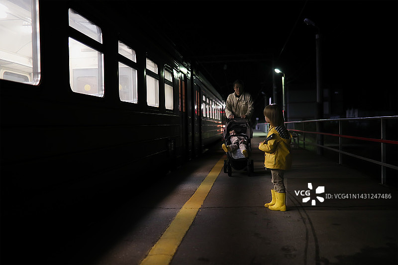 男人，带着孩子的成熟父亲，晚上在火车站台上推着婴儿车。有孩子的旅行。图片素材