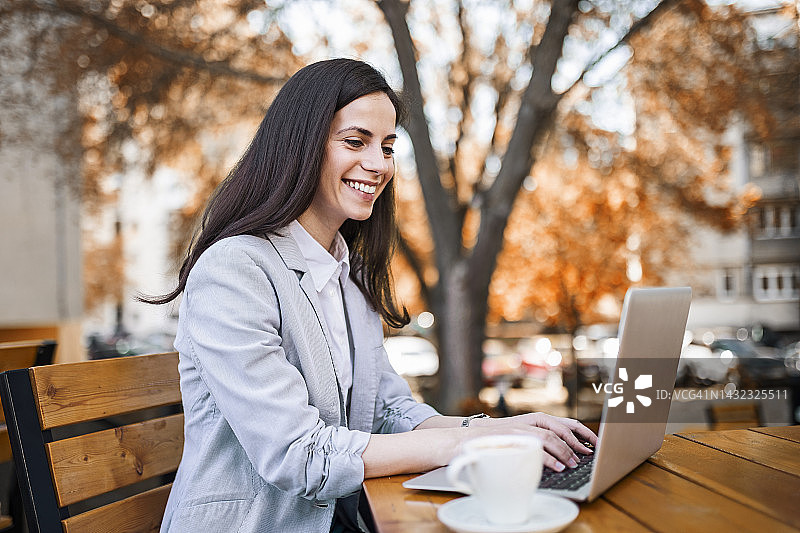 年轻的女商人坐在路边的咖啡馆里，喝着咖啡在笔记本电脑上工作图片素材