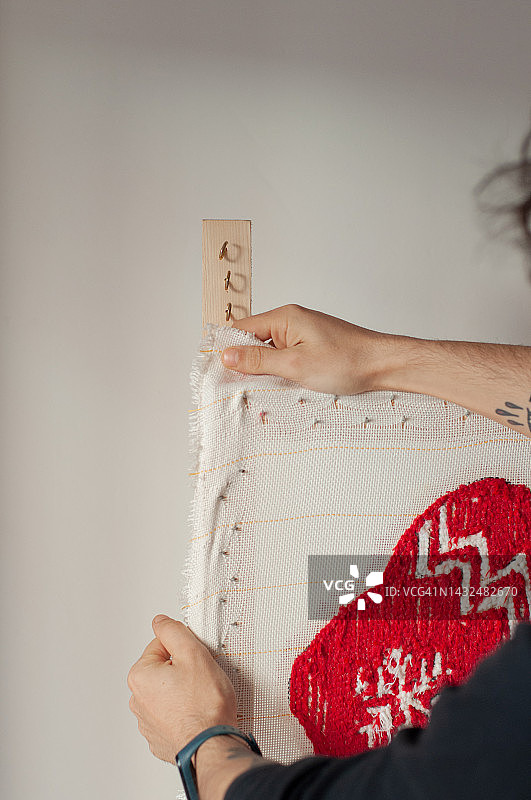 男人的手从框架上取下有机棉织物，制作成簇绒地毯，上面有圣诞老人的袜子和红色雪花的圣诞主题。垂直格式和自然光。图片素材