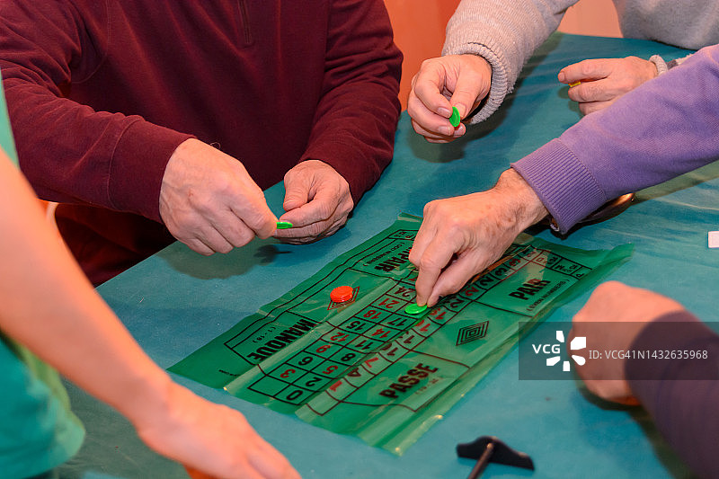 一群老年人在一个舒适的公寓里玩轮盘赌游戏，参加社交活动。图片素材