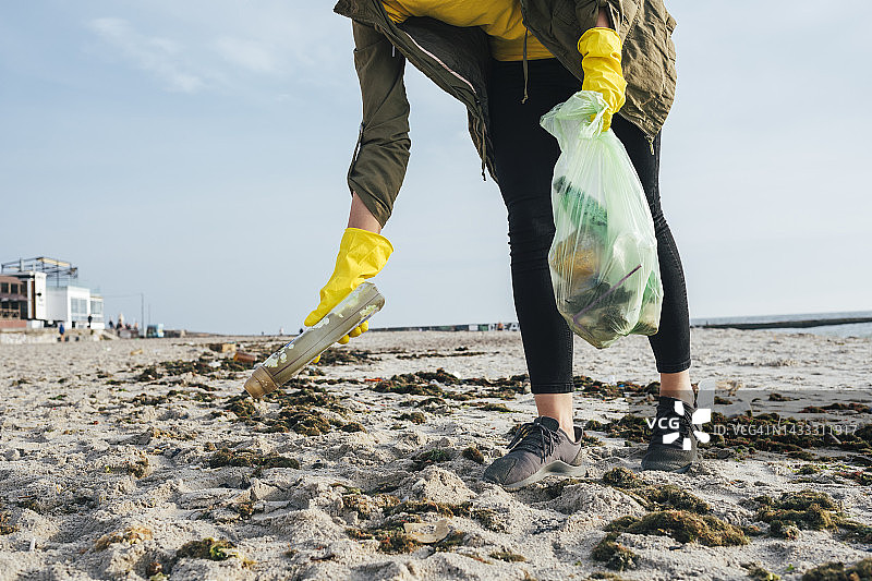 义工在海滩用垃圾袋收集沙中的废物图片素材