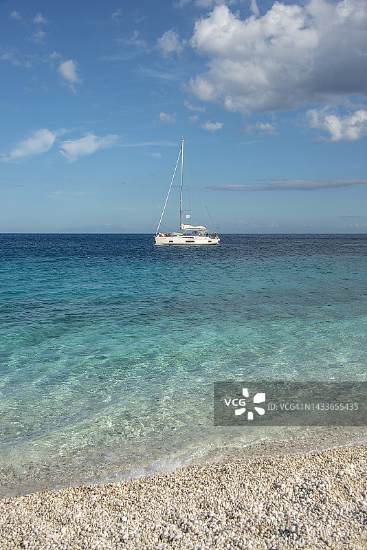 孤独的白帆双体船漂在平静的海面上。纯净浅蓝湛蓝的海湾水美丽的海滩，凯法罗尼亚，希腊图片素材