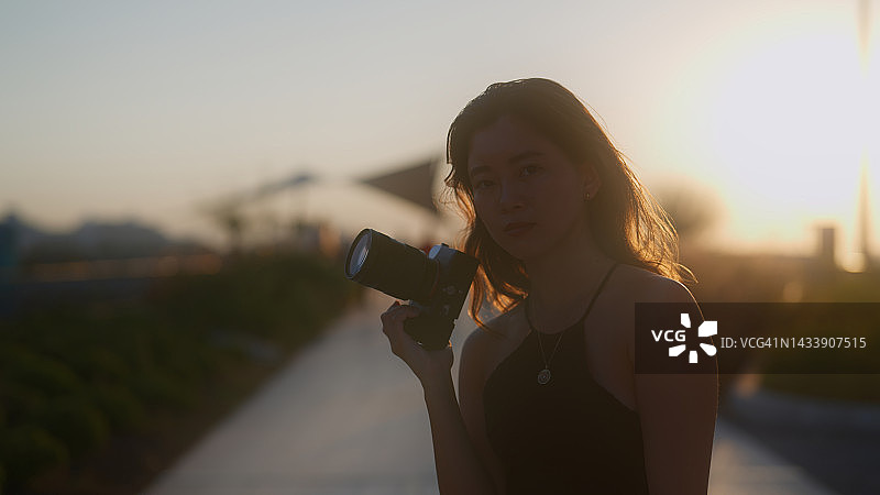 夕阳西下，年轻的女游客拿着相机，开心地看着相机图片素材