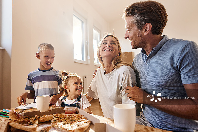 在新家打开行李后，幸福的一家人正在吃披萨。图片素材