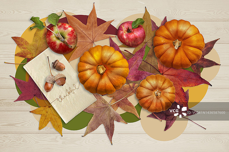 苹果、南瓜、橡子放在写着“感谢”的餐巾上，落叶放在浅色的木头背景上。前视图。感恩节秋天背景。图片素材