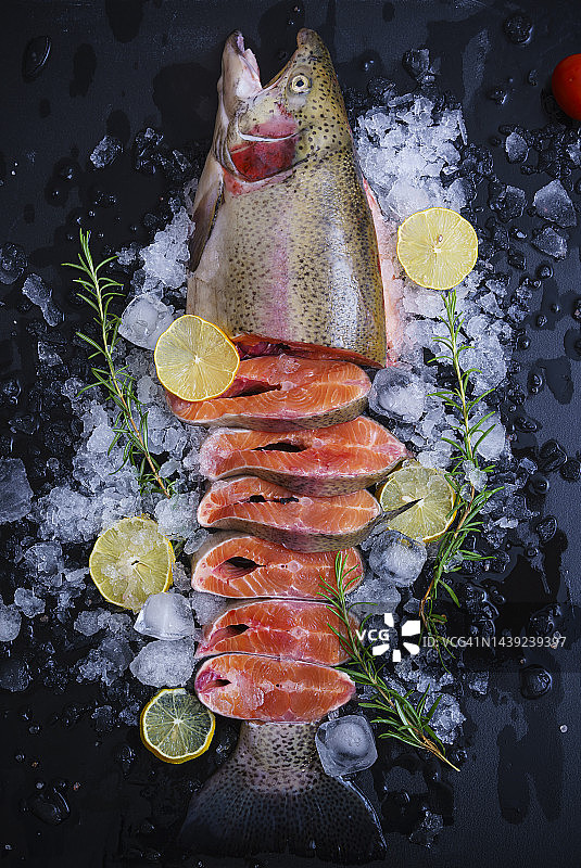 新鲜的生鲑鱼放在冰块上，用柠檬片、香草和蔬菜装饰在黑色的木制背景上图片素材
