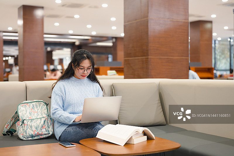 年轻女大学生坐在图书馆用笔记本电脑在线学习图片素材