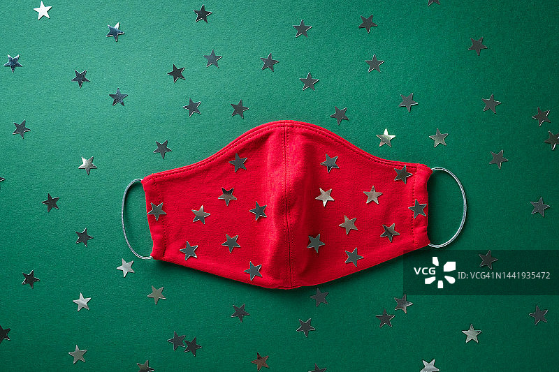 红色医用防护口罩和绿色圣诞背景上的五彩纸屑。预防和预防COVID - 19大流行的传播。防止病毒、感染和肺炎。快乐健康圣诞节的概念。图片素材