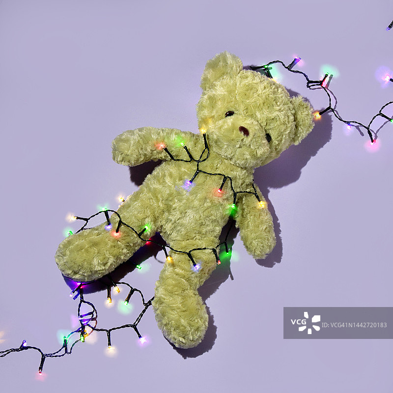 圣诞派对的创意布局与绿色泰迪熊和彩色圣诞灯串在柔和的紫色背景。八九十年代复古时尚美学派对概念。最小的新年庆祝想法。图片素材