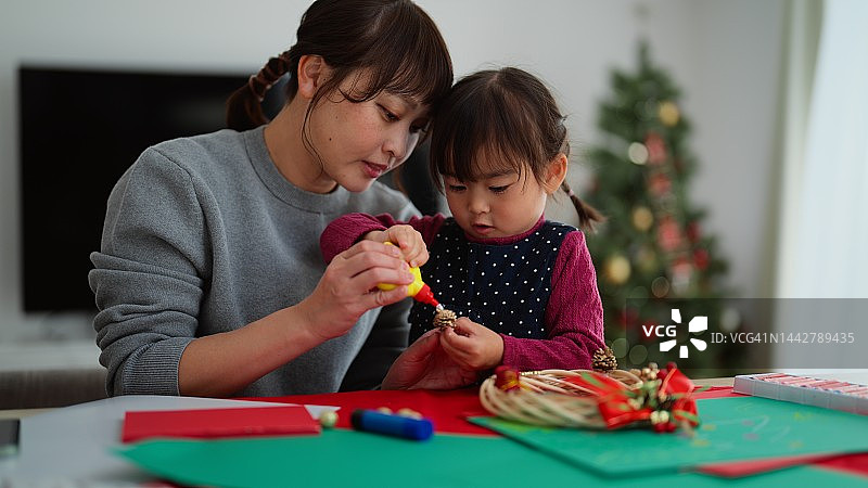 母亲和她学龄前的小女儿在家里的客厅里手工制作圣诞装饰品图片素材