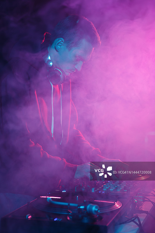 夜店DJ在嘻哈派对上表演。音乐节目主持人用混音器在烟雾中混音图片素材