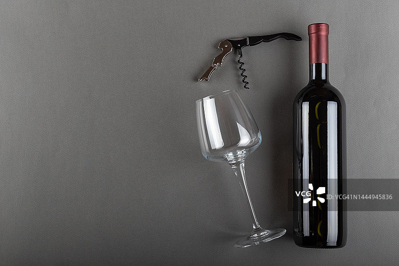 软木塞红色酒瓶，开瓶器和空酒杯在灰色背景。酒精饮料。酿酒的概念。图片素材