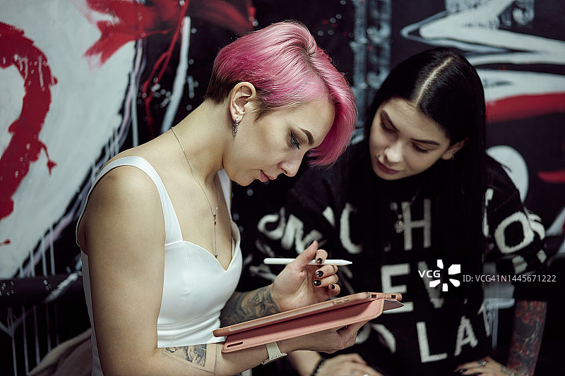 粉红色头发的年轻女子在笔板上为她的朋友画纹身图片素材