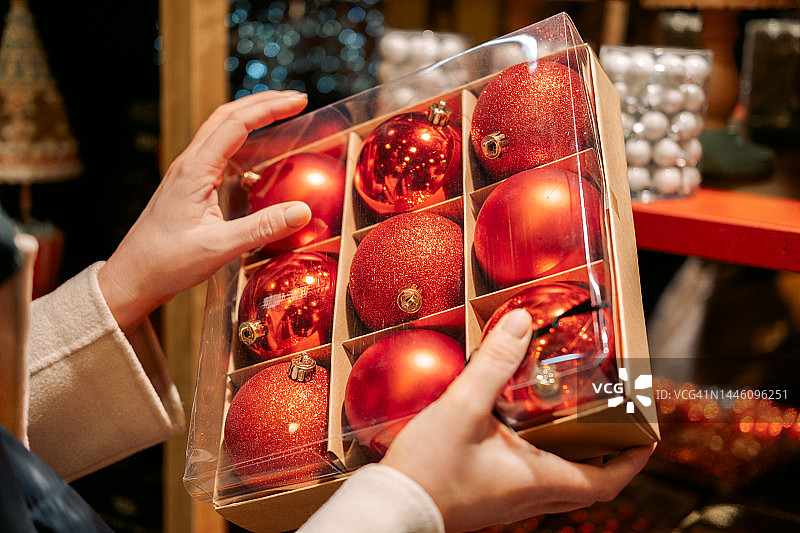 一个女人拿着一盒红色的气球，她正在为圣诞树选购圣诞和新年的装饰品图片素材