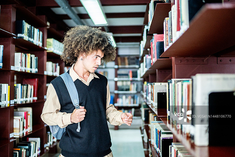 一个年轻的学生正在图书馆的书架上挑选一本书图片素材