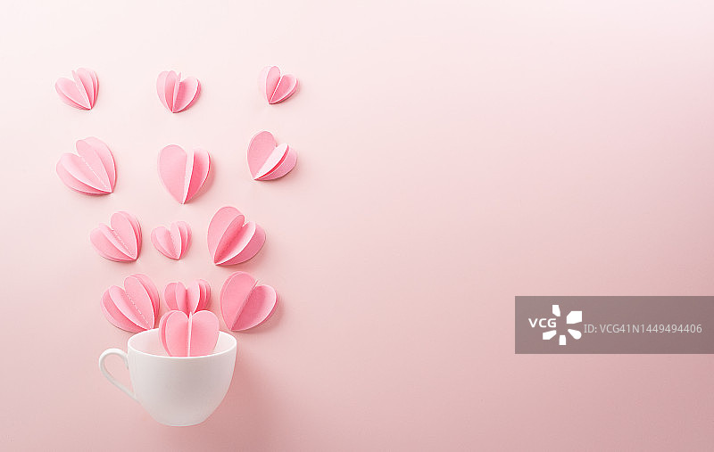 粉色的心形纸从白色咖啡杯中喷溅出来，背景是淡粉色的纸。爱情和情人节的概念。图片素材