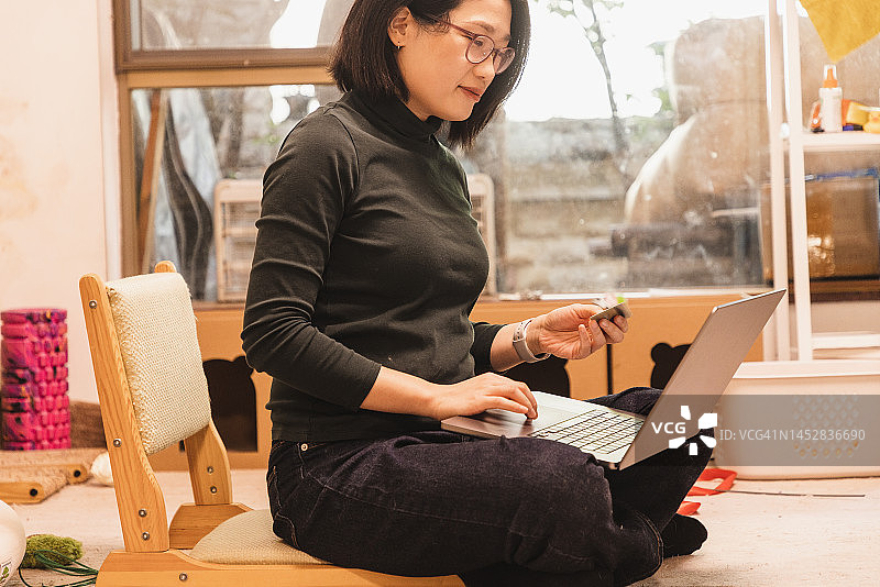 亚洲妇女在家里使用笔记本电脑时持有信用卡图片素材