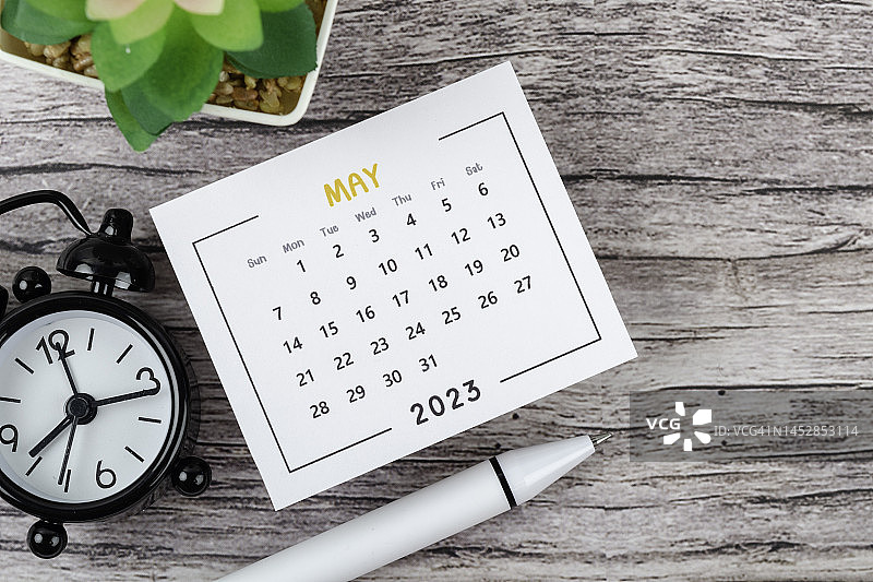日历桌2023:五月是组织者在木桌背景上用闹钟和白笔做计划和截止日期的月份。图片素材