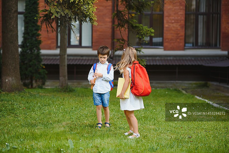 孩子们快乐地回到学校。小学生背着书包去户外学习。孩子们总是手拉手的。开始上课。秋天的第一天。一男一女是小学生。图片素材