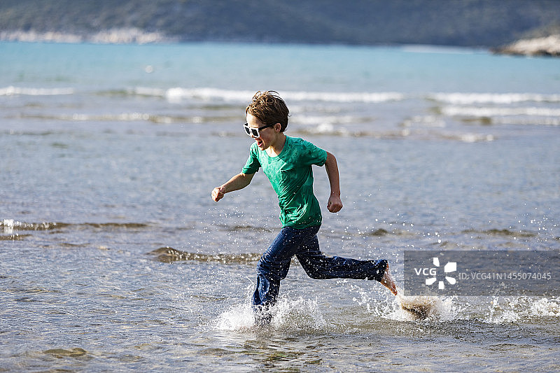 十几岁的男孩在沙滩上的水里奔跑图片素材